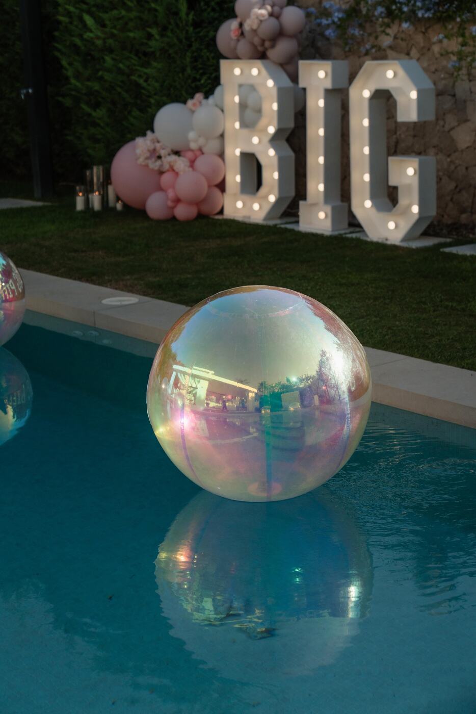 Iridescent orb floating in the pool at dusk in front of light-up BIG letters, Marbella