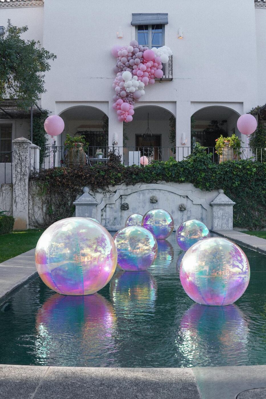 Iridescent orbz floating in a long pool in front of a villa with a pink balloon garland, Marbella