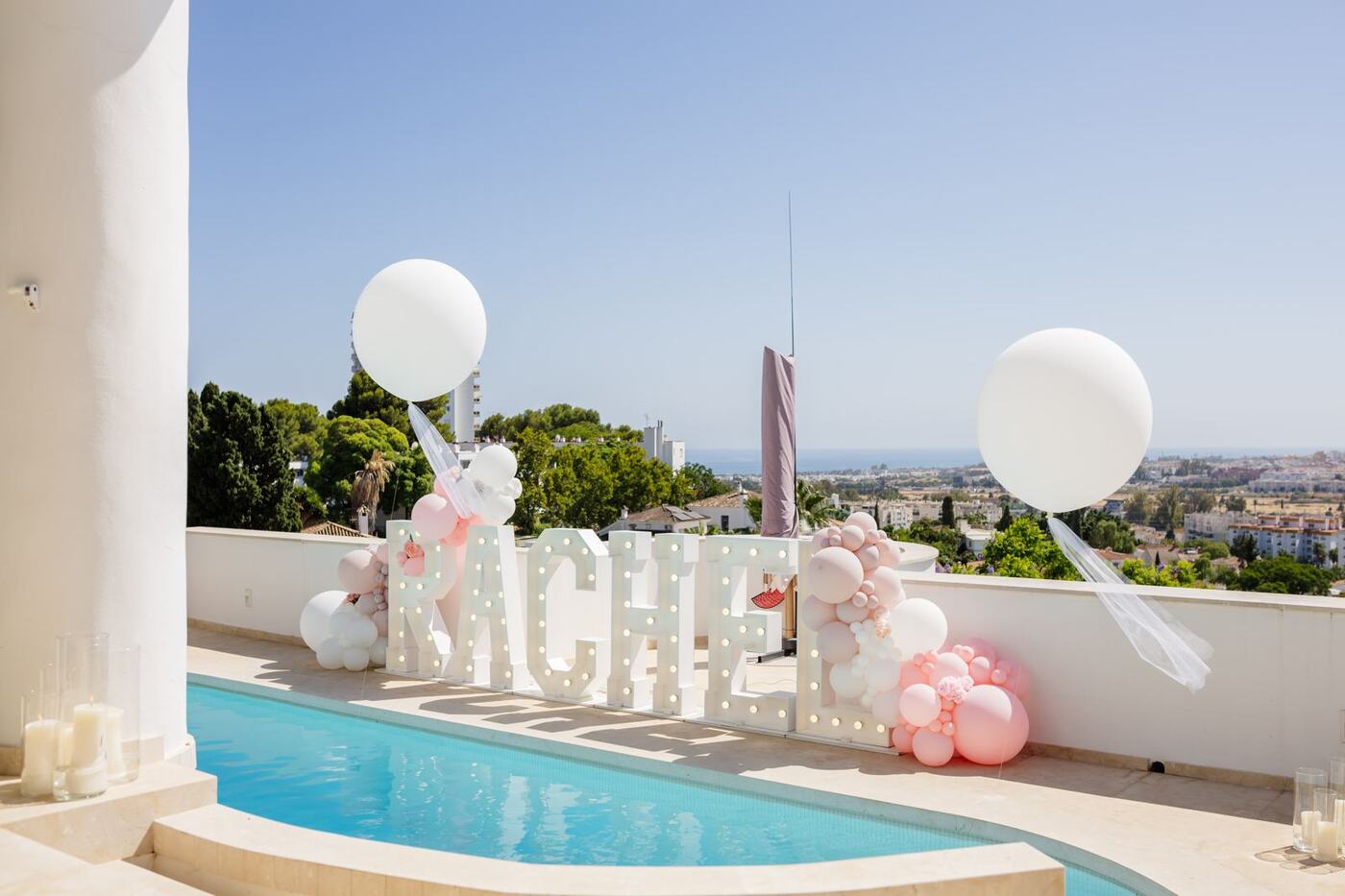 Light-up RACHEL marquee letters with pink balloons beside a pool, Marbella